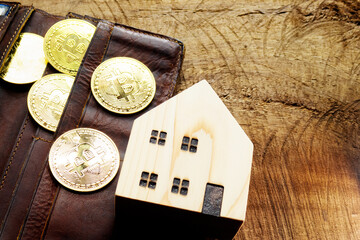 Many bitcoins are placed on brown leather wallet very shiny, which is surrounded by house model on wood table. Design concept for business, trading and Vintage tone