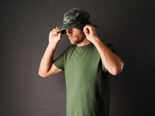 Fototapeta na wymiar The man is wearing a green camouflage Panama hat and a green t-shirt on a grey background.