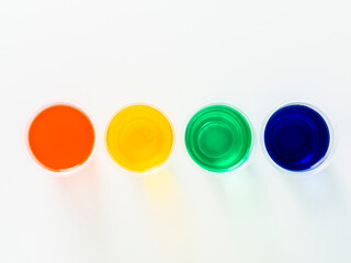 Four glasses with liquids of different colors on white background.