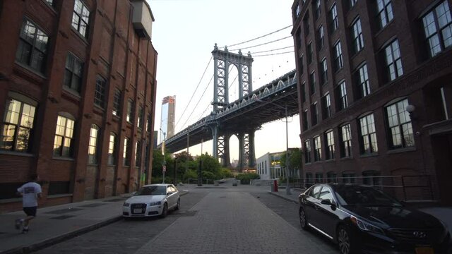 Brooklyn Bridge View from Dumbo with dumbo apartment houses and parked cars on the side in Summer in early morning light with Runner passing by 