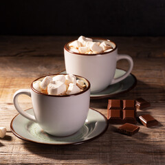Two cups of hot chocolate with cinnamon and marshmallow on wooden background