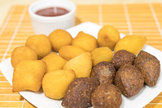 Salgadinhos fritos, saborosos, servidos em prato branco. Kibes de carne, coxinha de frango e risoles de queijo. Salgados para festas. 