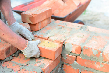 A mason person is bricklaying a wall of a new house from red bricks.