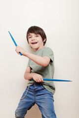 niño sobre fondo blanco hace la pose de tocar una batería con unas baquetas reales y una expresión alegre