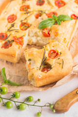 Traditional italian focaccia bread with tomatoes and rosemary in mental baking tray . On the beige brown paper and white concrete background.