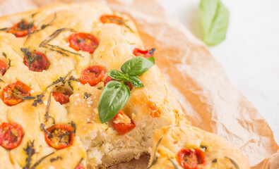 Traditional italian focaccia bread with tomatoes and rosemary in mental baking tray . On the beige brown paper and white concrete background.