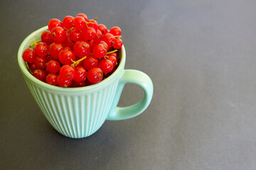 red currant berries in a turquoise Cup on a dark background side view . summer seasonal red berries