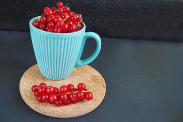 juicy red berries in a turquoise mug on a brown stand on a black table side view