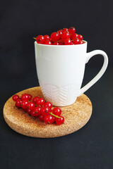 close-up of red currant berries in a white mug on a brown stand on a dark background side view . summer seasonal red berries