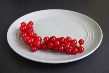 red juicy currant berries lie on a gray plate on a black background side view