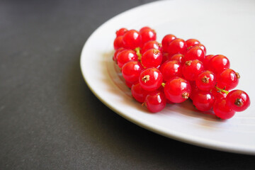 close up red juicy currant berries lie on a gray plate on a black background side view