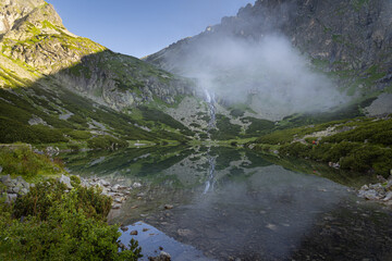 Sunrise in High Tatras mountains, Slovakia. Velicke Pleso (Velicke tarn), waterfall and hiking trail in morning. Top of a mountain illuminated by sunlight
