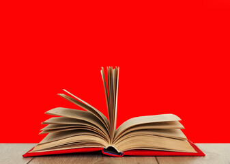 Open book textbook in a red cover on a wooden desk with red background. Back to school distance home education.Quarantine concept of stay home.