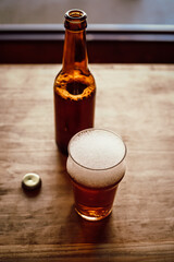 Opened beer bottle, bottle cap and glass with beer on an old wooden table