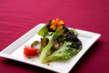 Elegant red romaine salad accented with strawberry slice, edible flower, and cheese