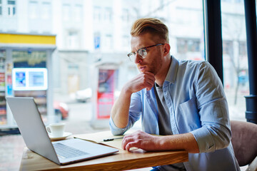 Thinking freelancer browsing laptop in cafe