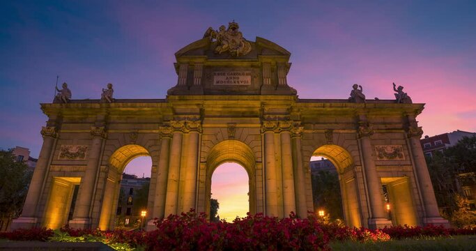 Puerta de Alcala famous monument in Madrid, Spain. Time lapse during sunset with beautiful colors and clouds. Flowers as foreground.