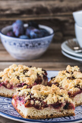 Three pieces of plum cake with crumble on a bluewhite plate on a wooden table