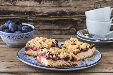 Three pieces of plum cake with crumble on a bluewhite plate on a wooden table