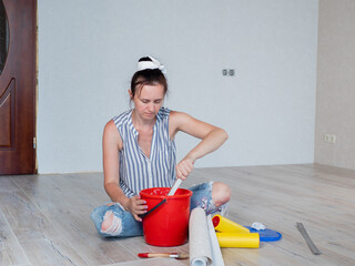 The woman in the room is sitting on the floor and stirring Wallpaper glue in a red bucket.