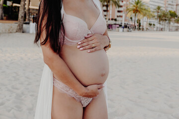 Fototapeta na wymiar Close-up of the belly of a young pregnant woman, dressed in a kimono and lingerie, on an empty beach in Mallorca 