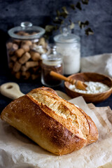 Homemade sourdough bread on a dark table with a napkin, next to flour. Loaf of freshly baked bread close up, vertical background