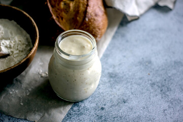 Bread starter sourdough in a glass jar on a dark background, near bread and flour, vertical background, close-up
