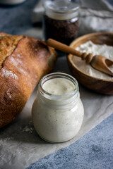 Bread starter sourdough in a glass jar on a dark background, near bread and flour, vertical background, close-up