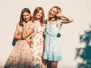 Three young beautiful smiling hipster girls in trendy summer sundress.Sexy carefree women posing on the street near wall. Positive models having fun and hugging - obrazy, fototapety, plakaty
