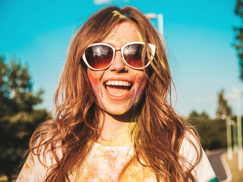 Happy beautiful woman after party at Holi colors festival in summer time.Young smiling girl having fun after music event at sunset. Positive model going crazy in sunglasses at sunset