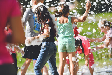Young people in the foam. A foam party. Group of children having fun, enjoying and dancing at a foam party in aqua park. Outdoor view of foam machine.