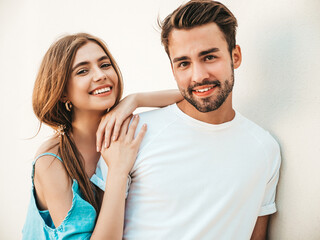 Portrait of smiling beautiful woman and her handsome boyfriend. Woman in casual summer jeans dress. Happy cheerful family. Female having fun. Couple posing near wall