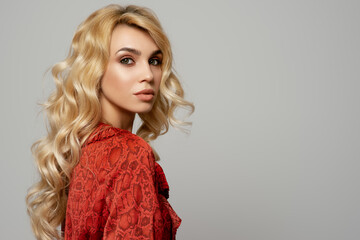 Beautiful confident blond woman with evening makeup, long waved hair, posing on grey background....