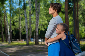 Excited schoolgirl hugs mom behind her back. The girl missed her mother very much.