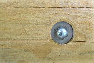 Detail of screwed parts of wooden parts of a garden house. Steel nut with a large round washer. Natural wooden planks connected with a steel screw.