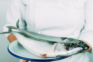 Woman in chef's clothes showing a dish with fresh fish. Kitchen concept.