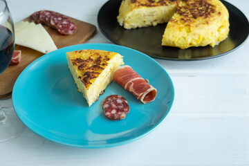 Spanish potato omelette with ham and sausage with cheese board and glass of wine on a white background. Typical food concept. Copy space.