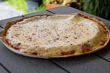 Freshly baked cheese pizza on outdoors wooden table with natural light