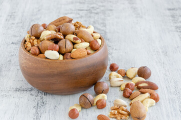 Fototapeta na wymiar Mix of nuts in a wooden bowl on a light wooden background. Healthy food concept. Horizontal, selective focus.