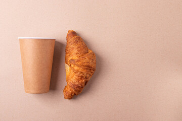 a cardboard coffee cup and a croissant on beige rustic background