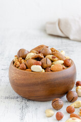 Mix of nuts in a wooden bowl on a light wooden background. Healthy food concept. Vertical, copy space.