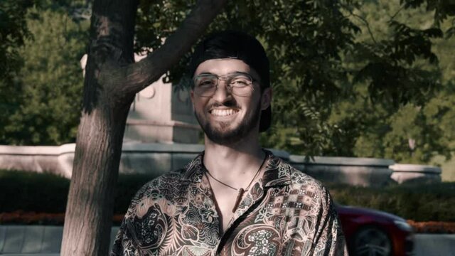 Plano medio retrato chico moderno caucasico con gafas, gorra negra y camisa colorida moderno con patines hipster estilo en el bosque y la carretera luz y sombras sonriendo feliz felicidad
