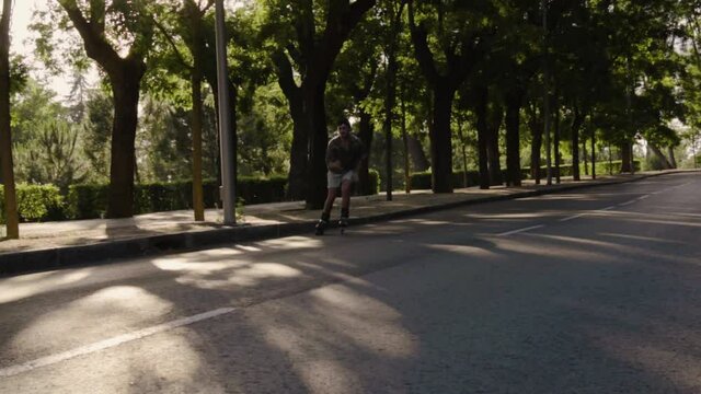 Plano medio  retrato chico moderno caucasico con gafas, gorra negra y camisa colorida moderno con patinando libre  libertad hipster estilo luz y sombras sonriendo bosque verde oscuro baialndo
