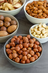 Hazelnuts, almonds, Brazilian nuts, cashews, macadamia, pecans and pistachios in bowls on a dark concrete background. Healthy food. Vertical, copy space.