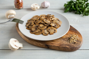 Appetizer of roasted slices mushrooms on a light plate on a wooden stand. Healthy vegetarian food close up on a white wooden background.