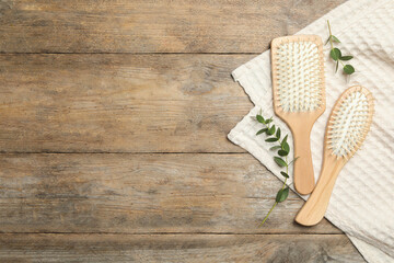 New hair brushes, twigs and towel on wooden background, flat lay. Space for text