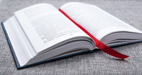 new open book on a gray table with a red ribbon bookmark - obrazy, fototapety, plakaty