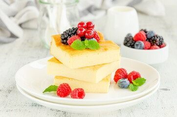 Homemade cottage cheese casserole with fresh berries and mint on top on a white plate. Healthy breakfast. Horizontal, copy space.
