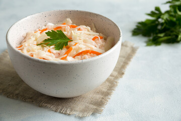 White ceramic bowl with homemade sauerkraut on canvas napkin. The dish is decorated with parsley. Close up on a gray, concrete background.