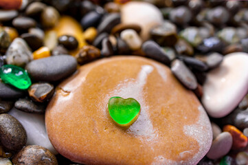 Fototapeta na wymiar Pebble stone background with small green transparent heart shaped pebble. Abstract. Valentine's Day